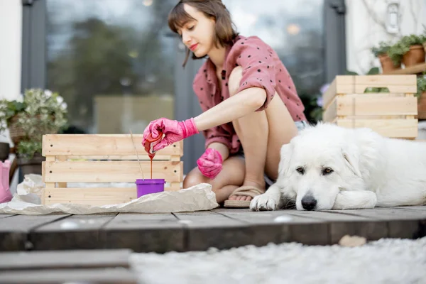Жінка малює дерев'яну коробку, сидячи з собакою на терасі — стокове фото