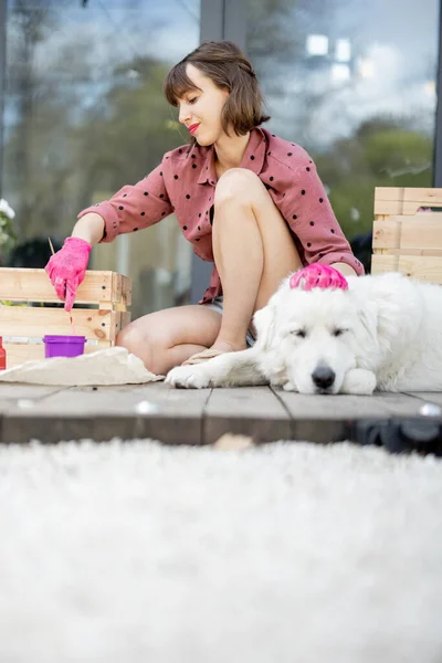 Woman painting wooden box, sitting with dog on terrace — Stock Photo, Image