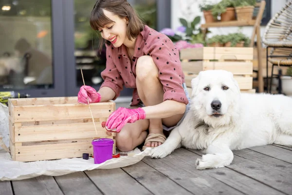 Kvinna målning trälåda, sitter med hund på terrassen — Stockfoto