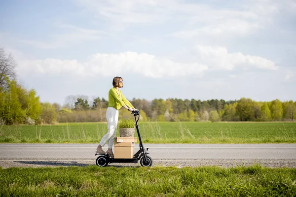 Woman driving electric scooter with parcels on the field road — Stok fotoğraf