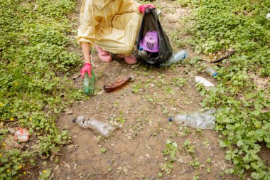 Ormanda dağınık plastik çöpleri toplayan bir kadın.
