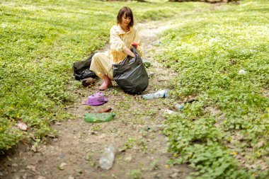 Ormanda dağınık plastik çöpleri toplayan bir kadın.