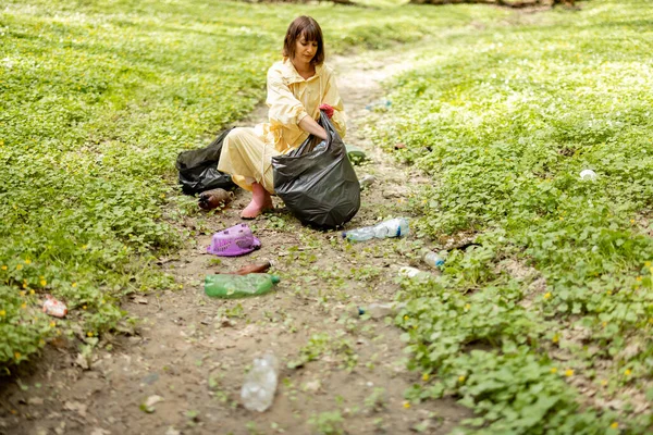 Ormanda dağınık plastik çöpleri toplayan bir kadın.