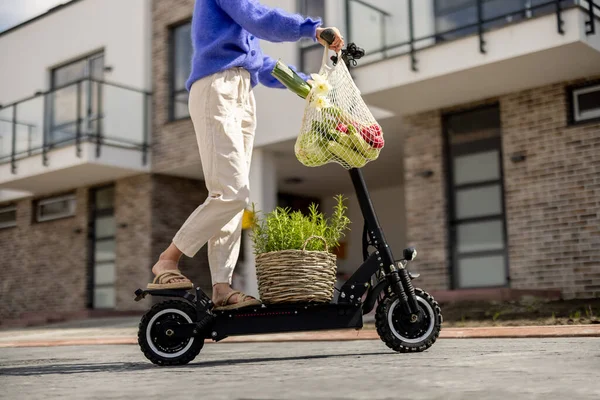 Woman going home with fresh vegetables on electrical scooter — стоковое фото