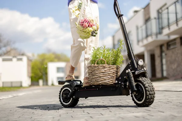 Kadın eve elinde taze sebzelerle elektrikli scooterla gidiyor. — Stok fotoğraf