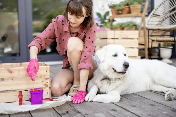 Woman painting wooden box, sitting with dog on terrace — Fotografia de Stock