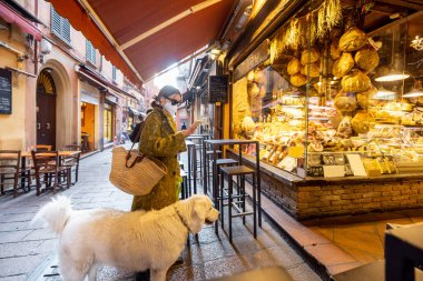 Tıbbi maskeli bir kadın köpeğiyle Bolonya 'daki yemek dükkanının yanında.