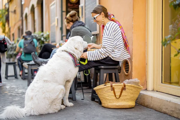 Kvinnan bryr sig om sin hund medan hon äter pasta på kaféet utomhus — Stockfoto