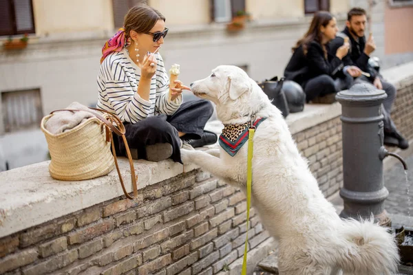 Kvinna äter glass medan hon sitter med hunden på en gata utomhus — Stockfoto