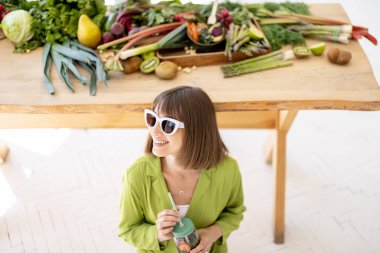 Kadın, arka planda sağlıklı yiyecekler olan limonata içiyor.