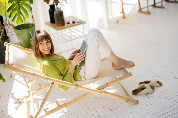 Vrouw zit ontspannen met een digitale tablet in de kamer met planten — Stockfoto