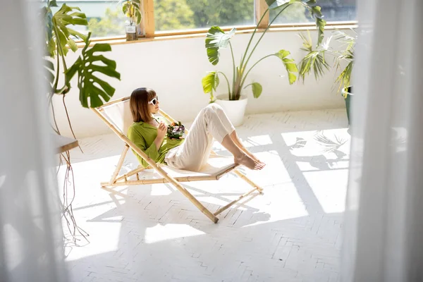 Женщина сидит расслабленной с напитком в комнате с растениями — стоковое фото