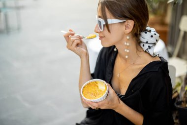Dışarıdaki restoranda Creme Brulee ile tatlı yiyen bir kadın.