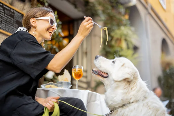 Restoranda tatlı beyaz köpeğiyle makarna yiyen bir kadın. — Stok fotoğraf
