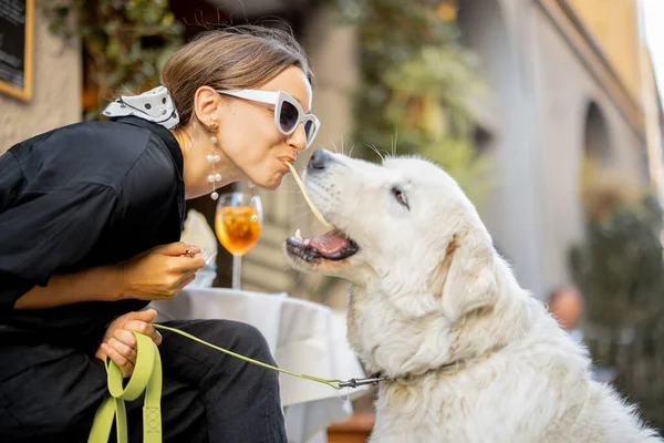 Kobieta jedząca makaron ze swoim słodkim białym psem w restauracji — Zdjęcie stockowe