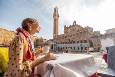 İtalya 'nın Siena şehrinin ana meydanında güzel manzaralı bir kafede kahvaltı yapan bir kadın.