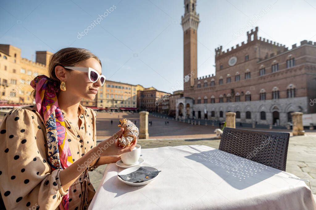 Woman having breakfast at outdoor cafe with beautiful view on main square of Siena city, Italy