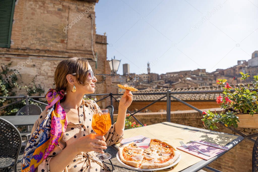 Young woman having lunch with pizza and wine at outdoor restaurant in Siena town