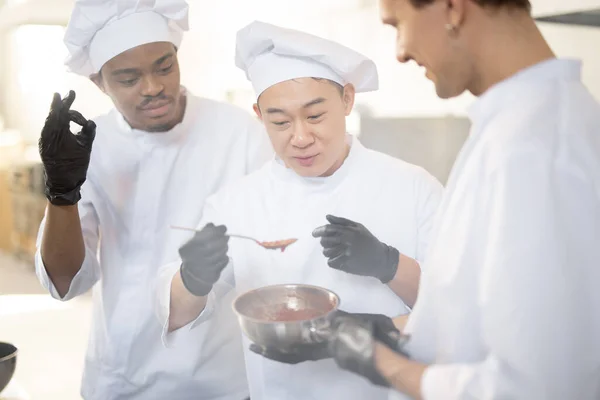 Chef cocina salsa degustación con una cuchara mientras cocina en la cocina — Foto de Stock