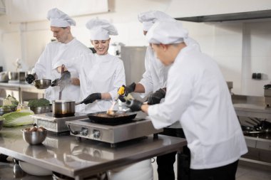 Üniformalı profesyonellerden oluşan çok ırklı bir ekip mutfaktaki bir restorana yemek hazırlıyor.