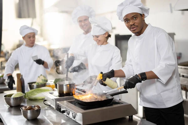 Equipo multirracial de cocineros profesionales en uniforme preparando comidas para un restaurante en la cocina —  Fotos de Stock