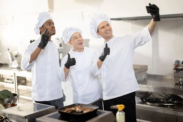 Feliz equipo multirracial de cocineros tomar foto selfie en el teléfono mientras cocinan juntos en la cocina — Foto de Stock