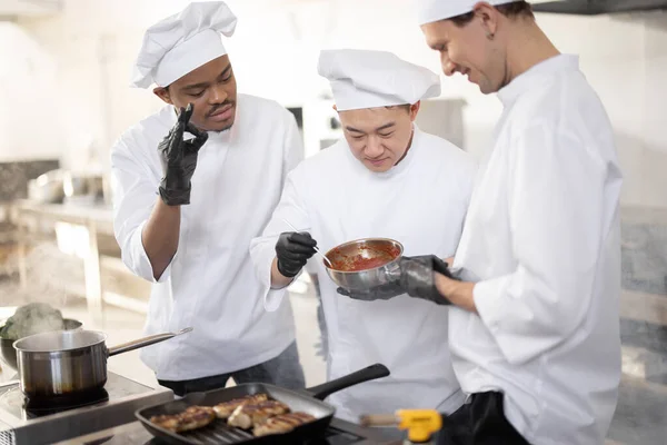 Chef kookt proeverij saus met een lepel tijdens het koken in de keuken — Stockfoto