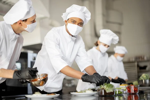 Grupo de cocineros terminando platos principales mientras trabajan juntos en la cocina —  Fotos de Stock