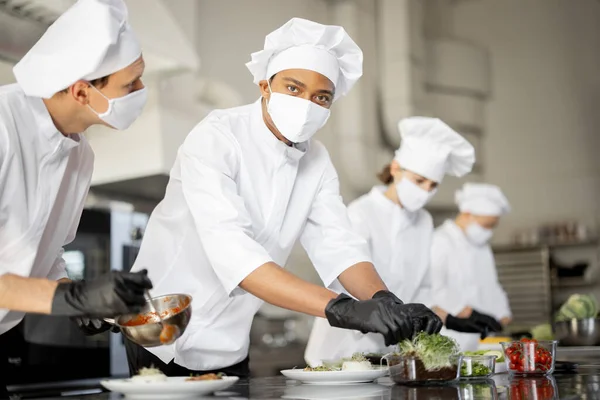 Grupo de cozinheiros terminando os pratos principais enquanto trabalham juntos na cozinha — Fotografia de Stock