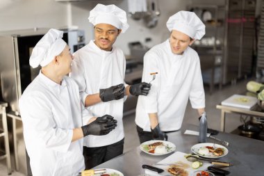 Farklı milletlerden aşçılar restoran menüsü için pişirilmiş yemekleri tadıyorlar.