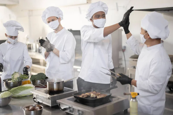 Équipe multiraciale de cuisiniers donnant cinq avec les mains l'un l'autre, tout en cuisinant dans la cuisine professionnelle — Photo