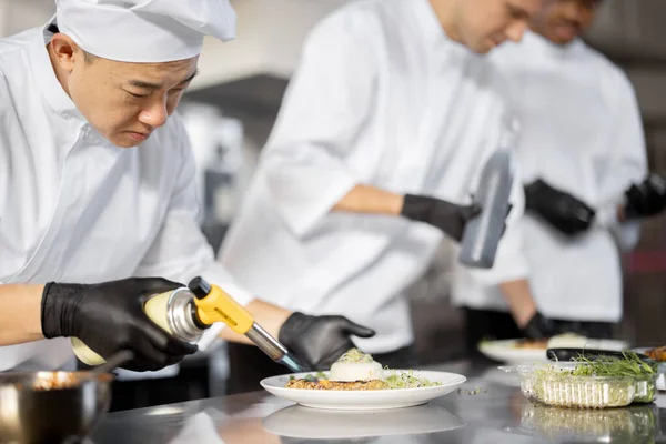 Group of cooks finishing main courses while working together in the kitchen — Stock Photo, Image