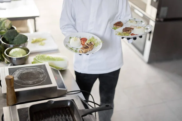 Chef segurando três pratos com refeições prontas na cozinha — Fotografia de Stock