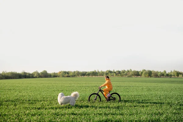 Young Person Yellow Overalls Rides Bicycle Dog Running Green Field — Stockfoto