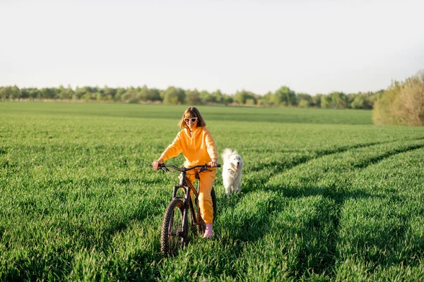 Young Happy Woman Yellow Overalls Rides Bicycle Dog Running Green — Stock fotografie