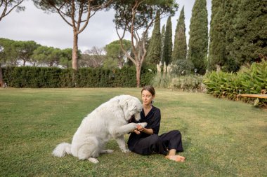 Young caucasian girl resting and caressing Maremmano-Abruzzese Sheepdog on green mediterranean lawn. Concept of weekend, tourism and vacation. Idea of friendship of human and pet. Sunny day