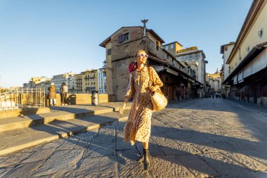 Floransa 'da Ponte Vecchio adında ünlü bir köprüde yürüyen bir kadın. Seyahat eden İtalyan simgeleri kavramı. Renkli şalı ve güneş gözlüklü şık bir kadın. Gün doğumunda geniş görünüm