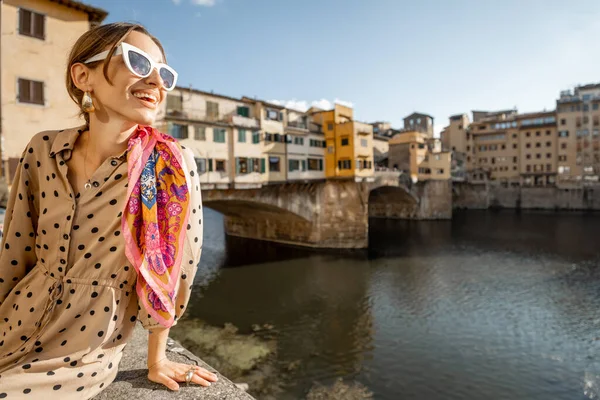 在佛罗伦萨著名的老桥上 年轻的女子欣赏着美丽的风景 夕阳西下坐在河边 参观意大利地标的女性游客 穿着衣服和五颜六色的披肩的时髦女人 — 图库照片