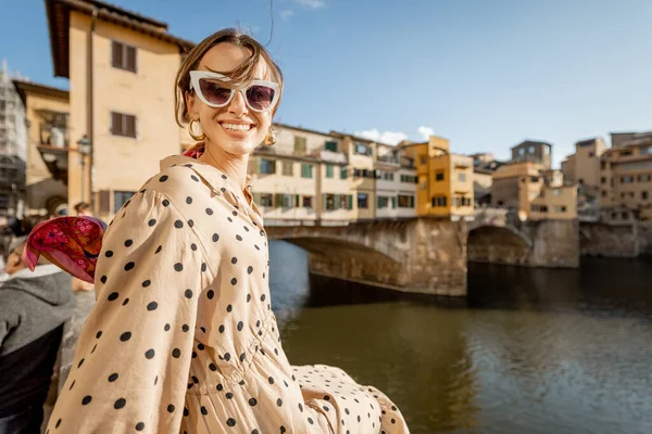 若い女性は 日没時に川沿いに座って フィレンツェの有名な古い橋の上に美しい景色を楽しんでいます イタリアのランドマークを訪れる女性旅行者 ドレスやカラフルなショールを身に着けているスタイリッシュな女性 — ストック写真
