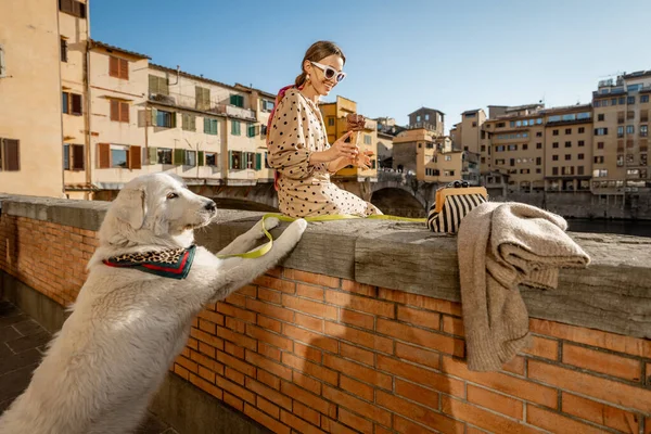 若い女性は有名なフィレンツェの古い橋の上で美しい景色を楽しみます 犬と一緒に座って 日没時に川沿いのアイスクリームを食べます イタリアのランドマークを訪れる女性旅行者 — ストック写真