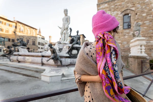Young woman traveling famous italian landmarks in Florence city. Enjoying beautiful architecture and Neptuine fountain on Signoria square. Woman dressed in Italian style with colorful scarf and hat