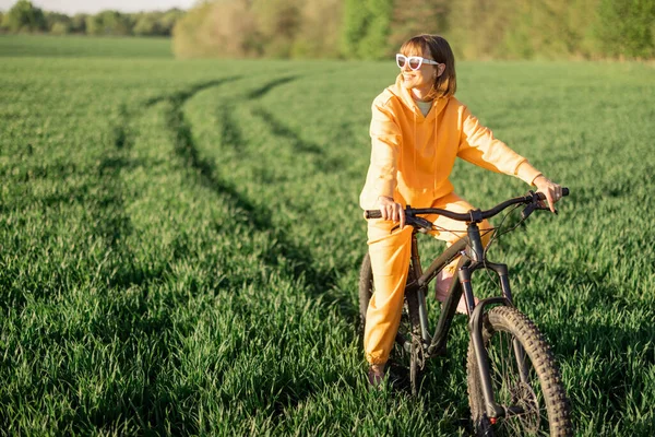 Mladá Žena Oranžové Kombinéze Jezdí Kole Zelené Louce Během Západu — Stock fotografie