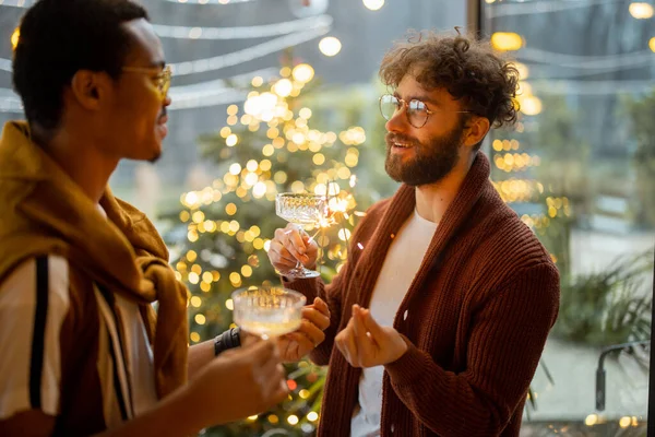 冬の休暇を祝う2人の男性の友人は 裏庭でワインと一緒に立っています 背景にクリスマスツリー 白人とヒスパニック系の男が一緒に ゲイのカップルや休日の気分のアイデア — ストック写真