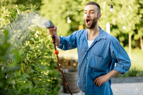一个英俊的家伙在花园浇灌绿色的树篱 丈夫在自家后院照看灌木丛 — 图库照片