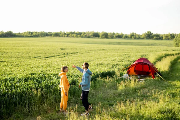 夏の間 緑のフィールドでテントと一緒に旅行しながら 若いカップルは楽しみ 話し合います — ストック写真