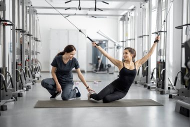 Rehabilitasyon uzmanının yardımıyla basınç azaltma simülatörleri üzerinde egzersiz yapan genç bir kadın. Sağlık ve iyileşme için fizik tedavi kavramı. Geçmişin tedavisinde kineziyoloji fikri