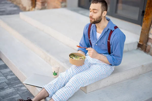 一个时髦的家伙吃着健康的食物从一个碗里拿走 而在午餐的时候坐在街上 健康的素食主义者工作生活方式的概念 — 图库照片