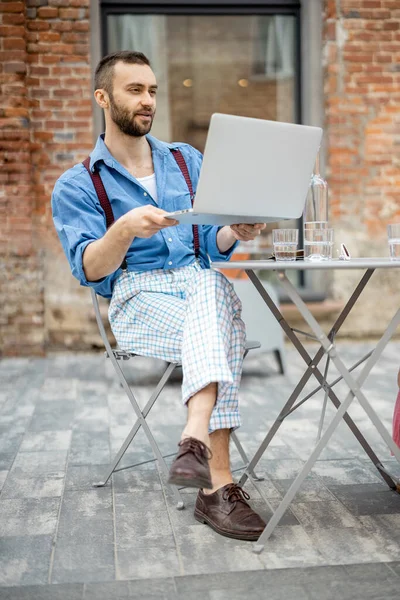 スタイリッシュなビジネスマンは 現代のカフェテラスに座っている間 ラップトップ上でオンライントークを持っています フリーランスとオンラインの仕事の概念 — ストック写真