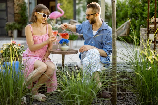 年轻貌美的夫妇在他们美丽的乡村别墅后院 坐在圆圆的咖啡桌旁 一边喝酒 年轻男女有一个浪漫的夜晚 — 图库照片