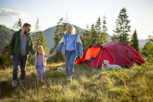 年轻的高加索家庭和小女孩一起走在绿色的草地上 带着帐篷在山上旅行 在营地度过一个快乐的家庭暑假 — 图库照片